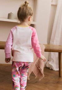 Kinderoutfit bestehend aus einem weißen Shirt mit pinken Raglanärmeln und einem gelben Halsauschnitt, kombiniert mit rosa Hosen, die mit bunten Mustern verziert sind.