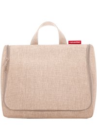 Beige Reisekosmetiketui aus strukturiertem Stoff, mit Reißverschluss und einem Griff an der Oberseite. Mit einem kleinen roten Markenlabel.