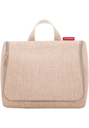 Trousse de maquillage de voyage beige avec un tissu texturé, fermeture éclair, et une poignée supérieure. Présente une petite étiquette de marque rouge.