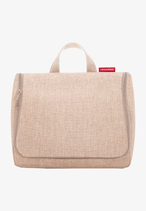 Beige Reisekosmetiketui aus strukturiertem Stoff, mit Reißverschluss und einem Griff an der Oberseite. Mit einem kleinen roten Markenlabel.