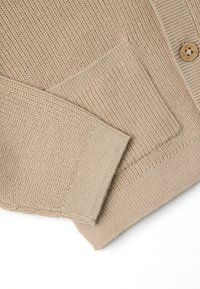 Beiger Cardigan mit strukturiertem Strick, ausgestattet mit einer Fronttasche und Holzknopfdetails, gerippten Bündchen und einem lässigen Schnitt.