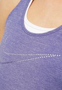 Fioletowy sportowy top na ramiączkach o melanżowej fakturze. Posiada biały wewnętrzny materiał oraz wzór logo w postaci kropek w kolorze srebrnym i czarnym.