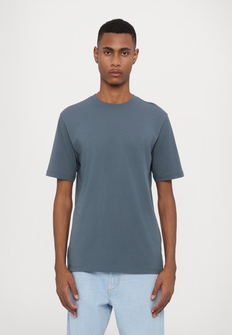 Kortærmet t-shirt med rund hals i mørkeblåt bomuld. Løs pasform med minimale syninger og glat tekstur. Kombineret med lyseblå jeans.