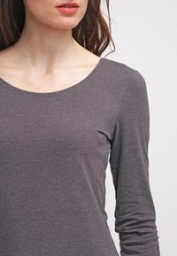 Haut à manches longues, gris foncé avec un col rond. Fabriqué dans un tissu lisse et extensible, avec une coupe ajustée qui épousera les formes du corps.