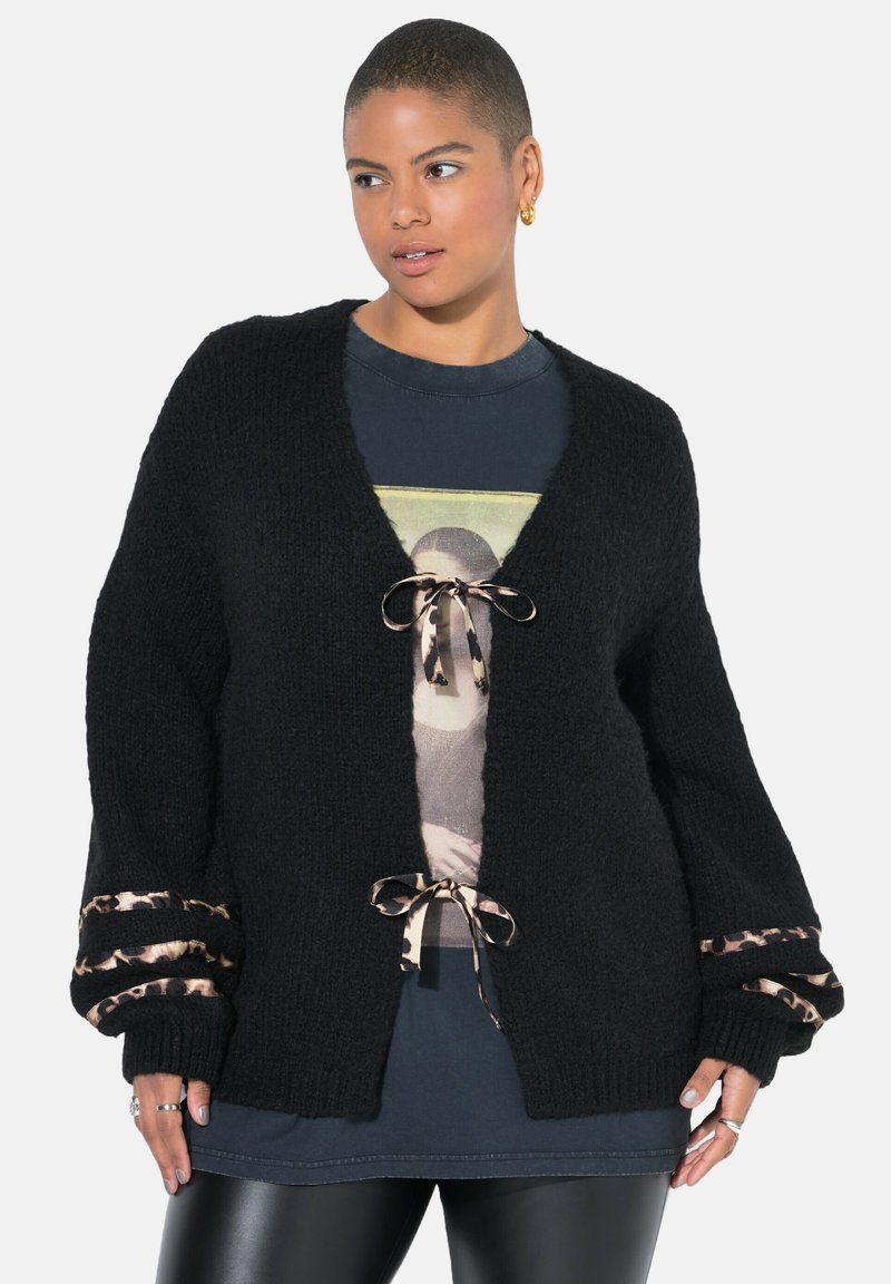Černý pletený cardigan s výstřihem do "V", leopardími potisky na rukávech a předními šňůrkami. Texturovaná látka dodává hloubku.