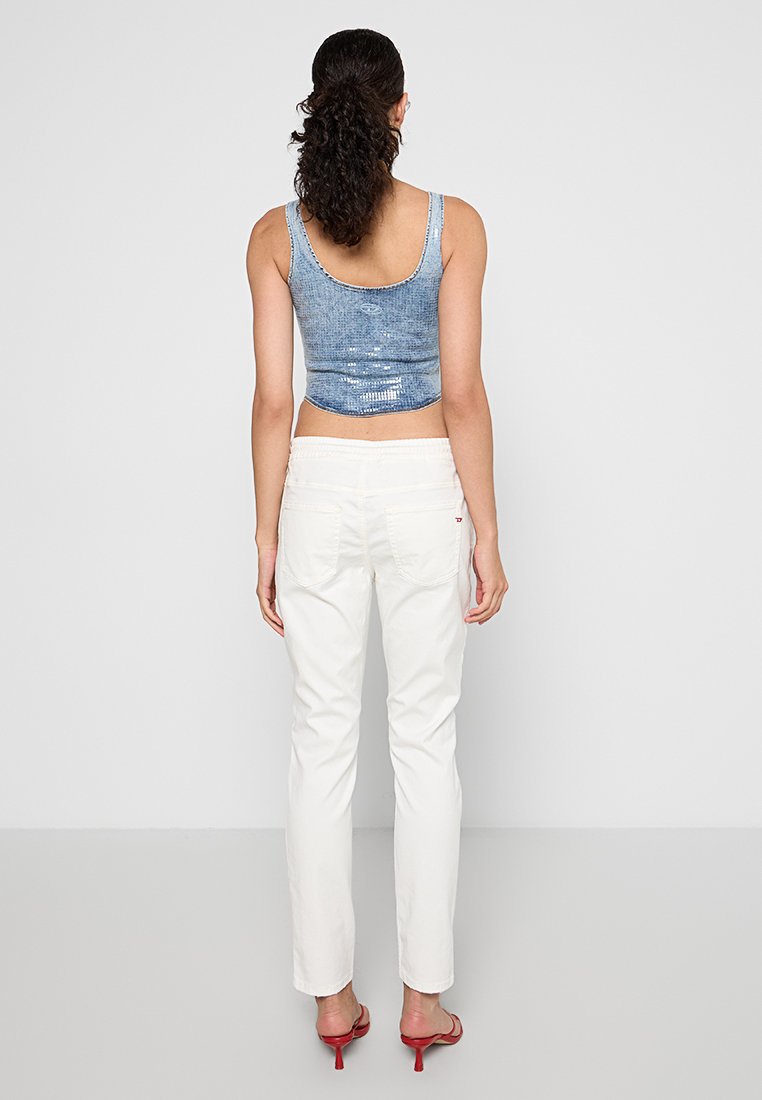 Getrimmtes, ärmelloses Oberteil aus blauer Denim mit strukturierter Oberfläche, kombiniert mit weißen, geraden Hosen und roten High Heels.