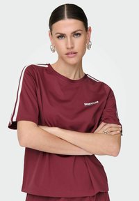 Burgunderfarbenes kurzärmliges Sport-T-Shirt aus leichtem Material. Mit weißen Streifen an den Ärmeln und einem Logo auf der Vorderseite.