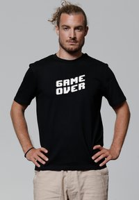 Zwart katoenen T-shirt met korte mouwen, voorzien van een pixelachtige "GAME OVER" grafiek in het wit op de voorkant. Casual pasvorm, eenvoudig ontwerp.