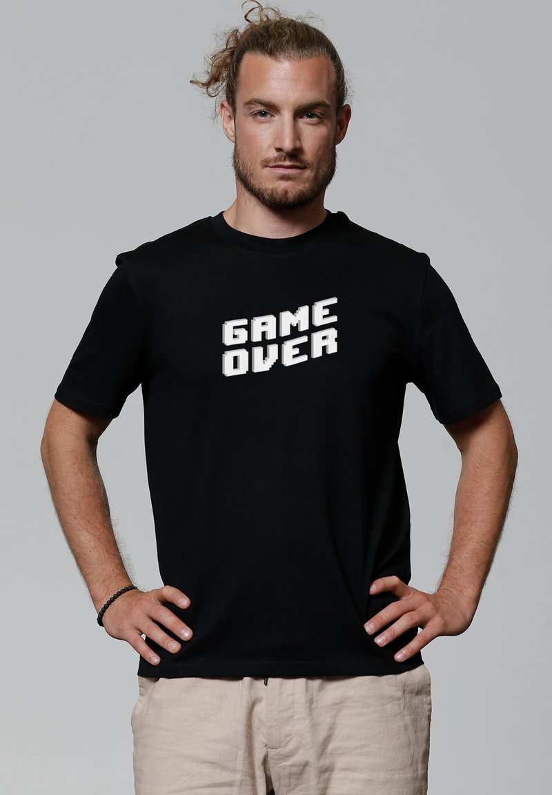 Zwart katoenen T-shirt met korte mouwen, voorzien van een pixelachtige "GAME OVER" grafiek in het wit op de voorkant. Casual pasvorm, eenvoudig ontwerp.