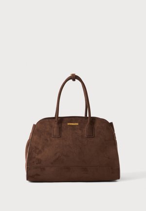 Sac à main en daim marron avec doubles poignées et logo doré "Steve Madden" centré en haut devant sur un fond clair uni.