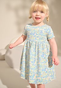 Blommig klänning med ett ljusblått och gult mönster, korta ärmar och vågig fåll. Materialet verkar vara lätt och luftigt.