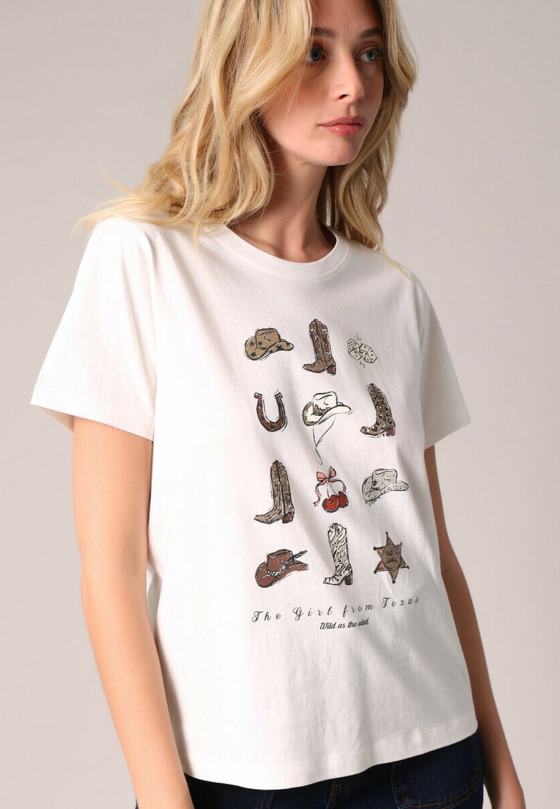 T-shirt en coton blanc arborant un graphique coloré de bottes de cow-boy, de chapeaux et d'un fer à cheval, avec le texte "La Fille du Texas."