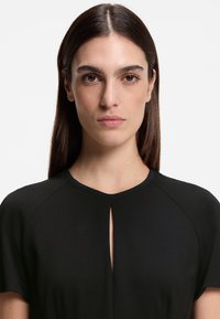 Μαύρο φόρεμα με στρογγυλή λαιμόκοψη και μικρό άνοιγμα στο μπροστινό μέρος. Κατασκευασμένο από απαλό ύφασμα με κοντά μανίκια και κομψό σχεδιασμό.