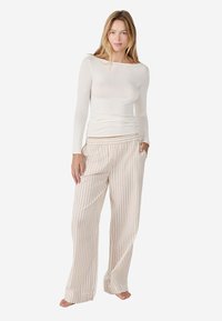 Lichtgewicht longsleeve top in een off-white materiaal, gecombineerd met een brede crème broek met verticale strepen en een knoopdetail.