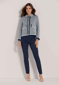 Geweven jasje in marineblauw en witte houndstooth, met een kraag, voorkruiden en een cropped snit. Gecombineerd met strak exemplaar marineblauwe broeken.