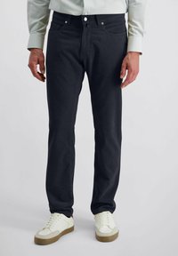 Dunkelblaue Jeans aus weichem Baumwolltwill, mit geradem Schnitt, fünf Taschen und silberfarbenen Beschlägen. Kombiniert mit weißen Sneakers.