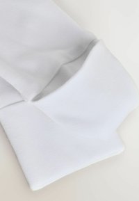 Weißer Baumwollstoff mit einer glatten Textur, der ein gefaltetes Manschettendetail zeigt. Einfaches, klassisches Design ohne sichtbare Muster oder Akzente.