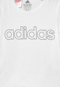 Bílý tričko Adidas pro děti ve věku 4-5 let s černým obrysem textu loga Adidas přes hrudník, velikostní štítek uvnitř límce.