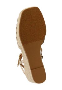 Sándalo beige con una suela de goma texturizada, que cuenta con un tacón de corcho y correas cruzadas. La parte inferior tiene un patrón ondulado para mayor tracción.