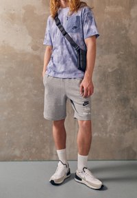 Light purple short-sleeve shirt with a chest pocket, gray shorts, white sneakers, and a black crossbody bag with adjustable strap.