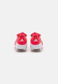 Rode voetbalschoenen hebben een gestructureerde bovenkant, een gevoerde kraag en een witte tussenzool met gouden studs. Het ontwerp bevat drie witte strepen op de hiel.
