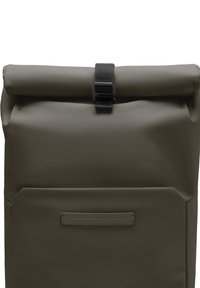Sac à dos à rabat vert en tissu texturé, avec une fermeture à boucle noire et une poche avant dotée d'un accent rectangulaire fin.