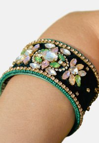Bracelet en velours noir orné de pierres précieuses multicolores, y compris vert, rose et transparent, avec des détails en perles complexes le long du bord.