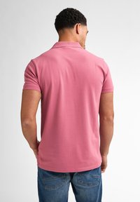 Polo à manches courtes en coton rose doux, avec un col classique et un ourlet droit, associé à un jean bleu pour un look décontracté.