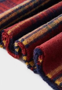 Red and navy plaid fabric, featuring yellow accents. Soft, textured wool with rolled edges, displaying a cozy, layered appearance.
