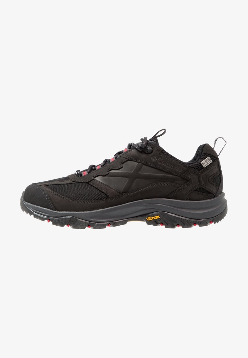 Chaussure de randonnée noire Columbia avec semelle grise, œillets rouges, adhérence Vibram et languette au talon, présentée de profil sur fond blanc.
