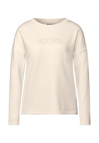 Langärmliges Creme-Hemd aus Baumwolle mit lockerer Passform, das in der Mitte einen dezenten, geprägten "ADORN MINDFULNESS"-Text zeigt.