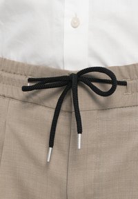 Harmaita kudottuja housuja, joissa on tekstuuripinta, etuosassa musta nauha solmittuna, täydentäen valkoista nappipaitaa ylhäällä.