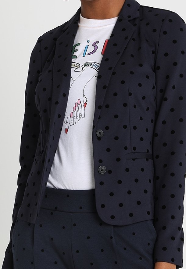 Marineblå kavaj med svarta prickar, kavajslag, två knappar och fickor, lagd över en grafisk vit t-shirt.