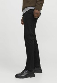 Black pants in a straight fit made from smooth fabric, paired with black lace-up shoes. The outfit includes a brown sweater layered over a striped shirt.
