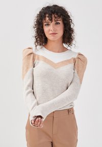 Suéter beige y crema con mangas abullonadas y textura en un patrón de zigzag. Presenta puños acanalados y una tela cómoda.