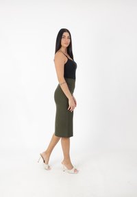 Top nero senza maniche, gonna midi verde oliva e sandali bianchi con punta aperta e dettagli dorati. Tessuto morbido e siluetta aderente.
