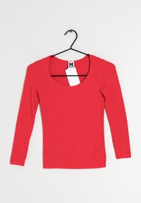 Röd ribbad långärmad tröja med djup rundad halsringning. Tillverkad av texturerad tyg, har en figurnära passform och hängs på en svart krok.