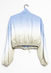Cropped jacket with a gradient from light blue to beige, featuring elasticated hem, long sleeves, and drawstrings. Smooth, shiny fabric texture.