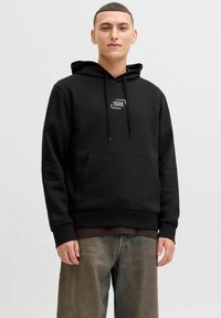 Sweat à capuche noir en tissu doux avec poche avant et capuche à cordon. Comprend une petite étiquette avec logo sur la poitrine.