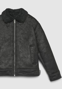 Giacca in shearling nero con zip frontale, colletto in lana, tasche laterali e dettagli con fibbia su colletto e orlo su sfondo chiaro.