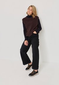 Maglione senza maniche in maglia marrone sopra una maglietta nera a maniche lunghe, abbinato a Jeans neri a gamba larga e sneaker nere e marroni.