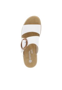 White sandal with two wide straps and a round brown buckle, featuring a soft tan insole with logo. Flat sole, casual design.