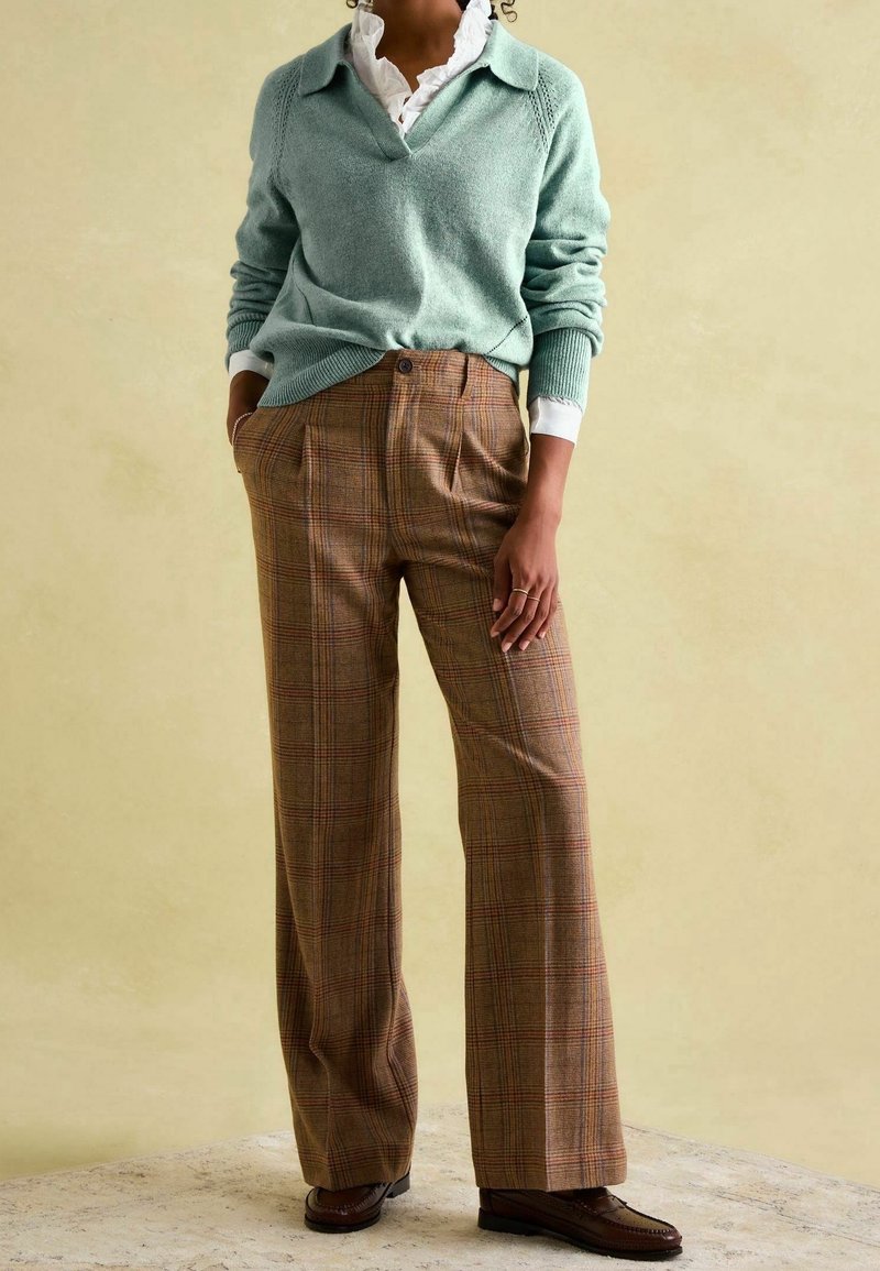 Pull en tricot vert clair avec un col en V et un col, associé à un pantalon taille haute marron à carreaux avec une jambe large et des plis. Mocassins marron.