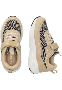 Baskets de sport beiges avec un motif zèbre noir et blanc, des accents dorés et des semelles blanches, dotées d'une sangle Velcro sécurisée.