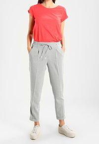 T-shirt corail à manches courtes associé à un pantalon gris clair à cordon de serrage, tapered, et des baskets beiges, sur fond blanc uni.