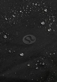 Waterdruppels die op zwarte gestructureerde stof liggen met een circulair logo in het midden, wat wijst op waterbestendig materiaal.