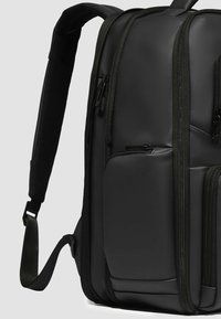 Zaino nero in tessuto strutturato, con più scomparti con zip, tasca laterale in rete e spallacci imbottiti e regolabili.