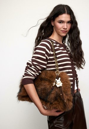 Ruskeasta tekoturkisesta käsilaukusta, jossa on kultainen ketjuhihna, ja jossa on kaniinimuotoinen koriste sekä helmiä. Laukku on suuri ja pörröinen.