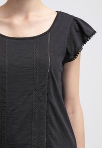 Czarny krótki top z krótkim rękawem, z zaokrąglonym dekoltem, fakturowanymi pionowymi paskami i delikatnym koronkowym wykończeniem przy rękawach. Miękka tkanina.