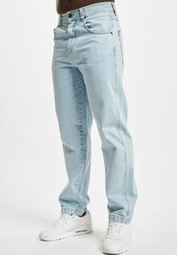 Light blue denim jeans with a relaxed fit, featuring front pockets and a button fly. Worn with white sneakers.